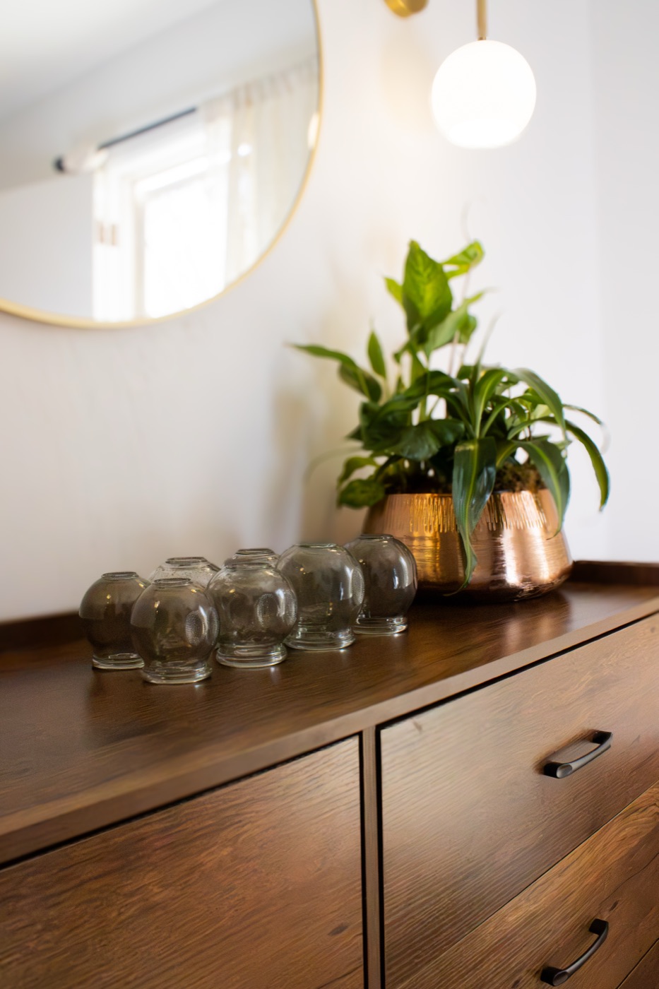 Glass cupping jars and a potted plant in a copper pot on a wooden dresser